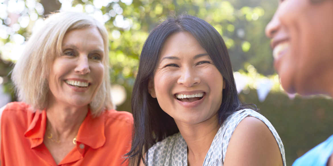 An asian woman in her 50's laughing, surrounded by a group of friends